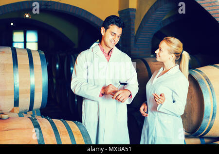 Friendly smiling diligent specialists in white robes checking ageing process of wine Stock Photo