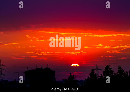Fire red urban sunset with black silhouette of light poles and houses of cityscape. Copy space. Red sunset background. Stock Photo