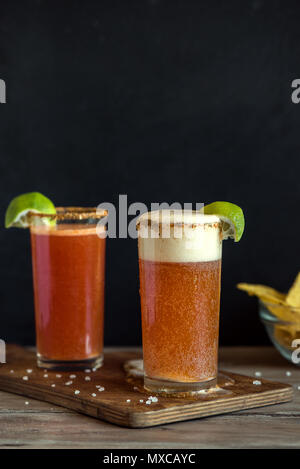 Michelada (Mexican Bloody Beer) with Spisy Rim and Tomato Juice served with Limes and Nacho Chips. Summer Alcohol Cocktail Michelada. Stock Photo