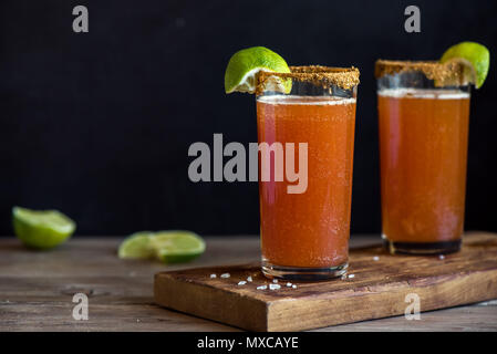 Michelada (Mexican Bloody Beer) with Spisy Rim and Tomato Juice served with Limes and Nacho Chips. Summer Alcohol Cocktail Michelada. Stock Photo