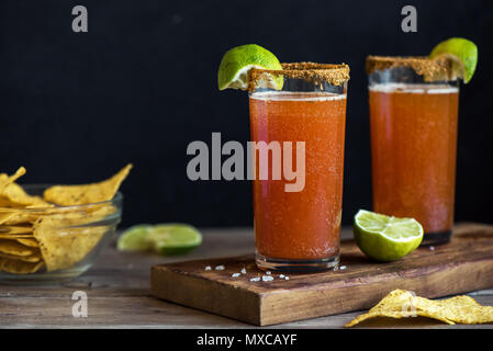 Michelada (Mexican Bloody Beer) with Spisy Rim and Tomato Juice served with Limes and Nacho Chips. Summer Alcohol Cocktail Michelada. Stock Photo