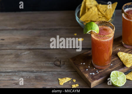 Michelada (Mexican Bloody Beer) with Spisy Rim and Tomato Juice served with Limes and Nacho Chips. Summer Alcohol Cocktail Michelada. Stock Photo