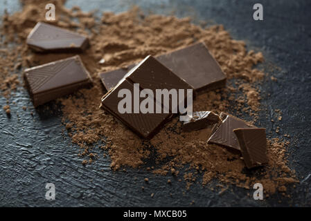 Broken chocolate pieces and cocoa powder on black. Chunks of chocolate onr dark stone background. Stock Photo