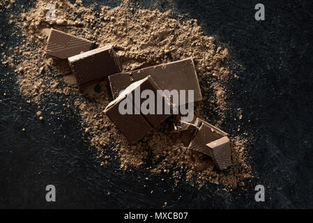 Broken chocolate pieces and cocoa powder on black. Chunks of chocolate onr dark stone background. Stock Photo