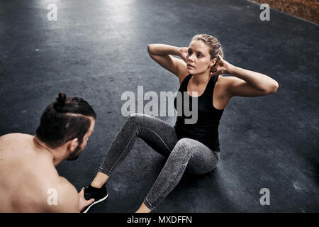 Fit young woman doing crunchees with her exercise partner on the floor of a gym during a workout session Stock Photo