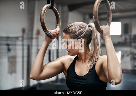 Fit young woman in a sporty tanktop getting focused during a workout session on rings at the gym Stock Photo