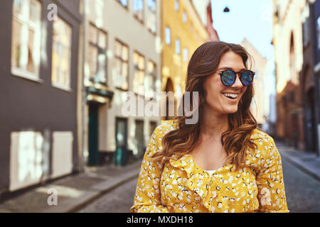 Smiling young brunette woman wearing sunglasses walking alone through the cobblestone streets of a city Stock Photo