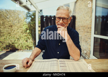 Content senior man sitting outside at his patio table and smiling while reading the newspaper and drinking a cup of coffee Stock Photo