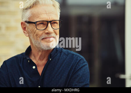 Senior man with a beard and wearing glasses smiling contently while standing by himself outside in his yard Stock Photo