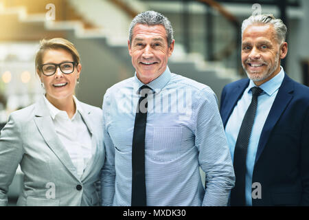 Smiling mature businessman standing in the lobby of a modern office building with two colleagues Stock Photo