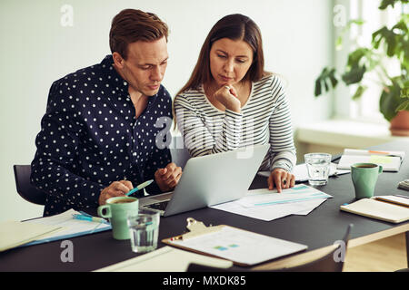Two focused business colleagues talking together over a laptop while sitting together at a desk in an office Stock Photo