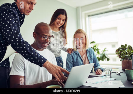 Smiling group of diverse businesspeople talking together over a laptop at a desk in an office Stock Photo
