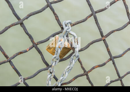 Close up of a Padlock and Chain on a wired Fence by the Sea Stock Photo
