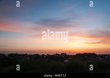 Wind turbines rising through the mist and silhouetted against the rising sun Stock Photo