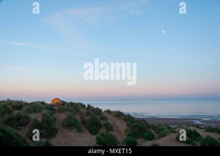 A tent perched on top of a sand dune at dawn Stock Photo