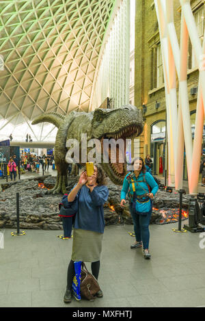A large model dinosaur promoting the Jurassic World film in the Kings Cross concourse with two women standing around it taking photos Stock Photo