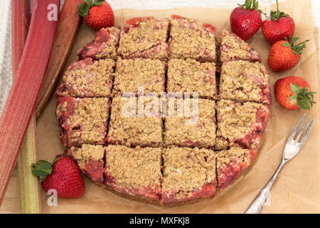 A delicious strawberry and rhubarb crumble slice, displayed with fresh fruit. Homemade and still warm from the oven. This recipe is gluten-free. Stock Photo