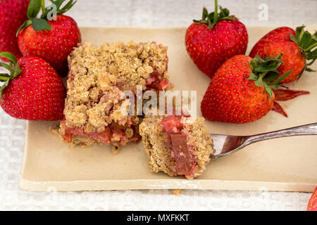 Healthy slices of red summer fruits bars served on a handmade ceramic plate. A delicious freshly baked dessert with strawberries and rhubarb. Stock Photo