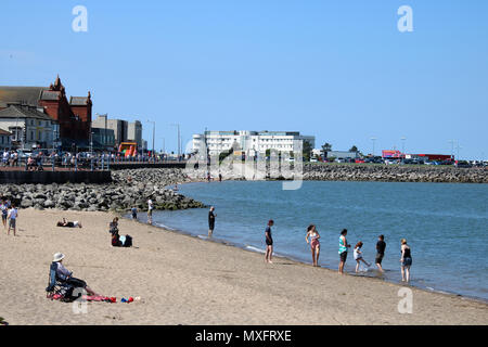 View along the seafront and beach towards the Midland Hotel in Morecambe, Lancashire, England with people enjoying the sandy beach at high tide. Stock Photo