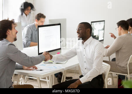 Diverse workers laughing shaking hands in shared workspace Stock Photo