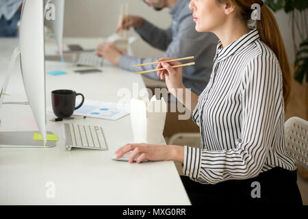 Focused female eating Asian food while working at desktop comput Stock Photo