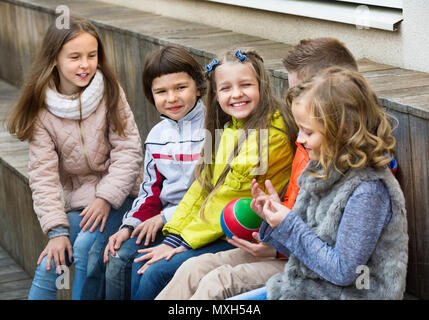 Group of cute children sitting on bench and sharing secrets outdoors Stock Photo