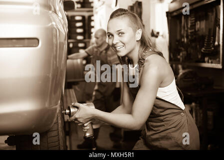 friendly smiling joyful female mechanic  working on car tyre assembling in service station Stock Photo