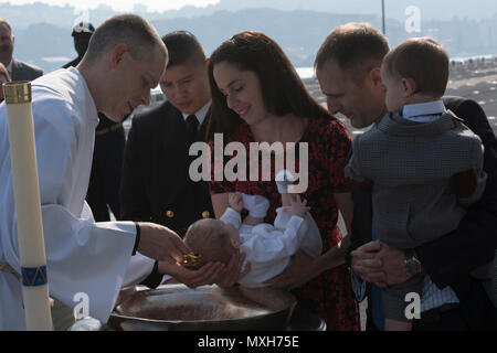 161105-N-XT039-165 SASEBO, Japan (Nov. 5, 2016) Lt. David Hammond (left), a chaplain aboard amphibious assault ship USS Bonhomme Richard (LHD 6), baptizes the son of Lt. Cmdr. Christopher Dike, the flight deck officer of Bonhomme Richard, on the ship’s flight deck. Bonhomme Richard, forward-deployed to Sasebo, Japan, is serving forward to provide a rapid-response capability in the event of a regional contingency or natural disaster. (U.S. Navy photo by Seaman Jesse Marquez Magallanes/Released) Stock Photo