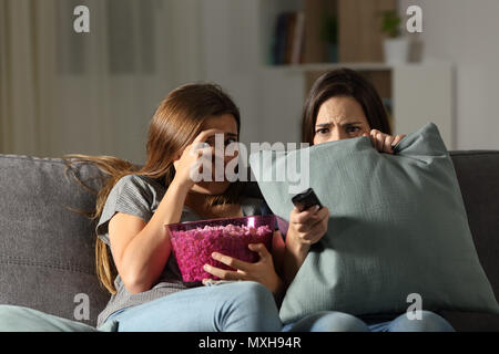 Terrified friends watching tv in the night sitting on a couch in the living room at home Stock Photo