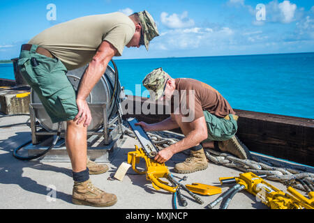 Chief Petty Officer Jesse Hamblin, right, and Petty Officer 1st Class Christopher Chilton, both assigned to Underwater Construction Team (UCT) 2’s Construction Dive Detachment Bravo (CDDB), replace the chain on a hydraulic chainsaw in Diego Garcia, British Indian Ocean Territory,  Nov. 8, 2016.  CDDB is performing precision underwater demolition and light salvage to remove obstructions from Diego Garcia's deep draft wharf. CDDB is on the third stop of their deployment, where they are conducting inspection, maintenance, and repair of various underwater and waterfront facilities while under Comm Stock Photo