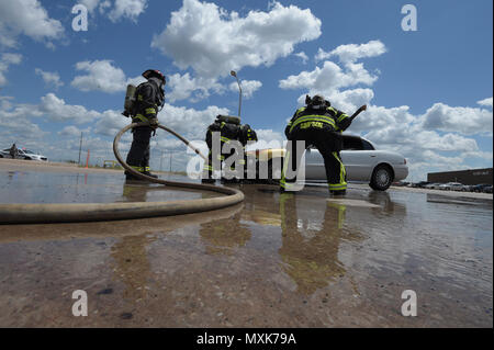 Members of the Tinker Fire and Emergency Services, 72nd Civil Engineer Squadron, work together to extinguish a vehicle fire May 4, 2017, Tinker Air Force Base, Oklahoma. William Green hoses the wheel-well of the car down while Capt. David Jones assists with the hose as Aaron Simpson, far right, stands-by with a fire-axe. The privately-owned vehicle developed mechanical trouble and caught fire near the Oklahoma City Air Logistics Complexs' building 9001. Stock Photo