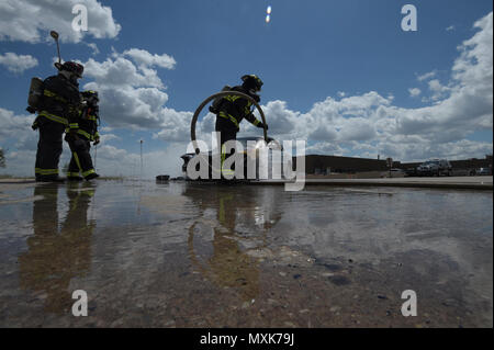 Members of the Tinker Fire and Emergency Services, 72nd Civil Engineer Squadron, work together to extinguish a vehicle fire May 4, 2017, Tinker Air Force Base, Oklahoma. William Green hoses the wheel-well of the car down while Capt. David Jones, left, and Aaron Simpson, background, stands-by as spotters. The privately-owned vehicle developed mechanical trouble and caught fire near the Oklahoma City Air Logistics Complexs' building 9001. Stock Photo