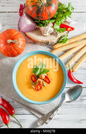Pumpkin soup with chili pepper, pumpkin seeds, croutons and parsley in blue bowl on white wooden background Stock Photo