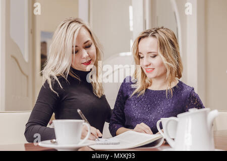 Two young women discussing documents and drinking tea at meeting in conference room Stock Photo