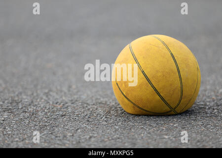 Right hand focus, close up of old tired deflated let down yellow basketball on a road surface concept. needs air, worn out spent and discarded sport Stock Photo