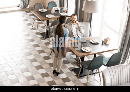 Waitress waiting while client talking on phone Stock Photo