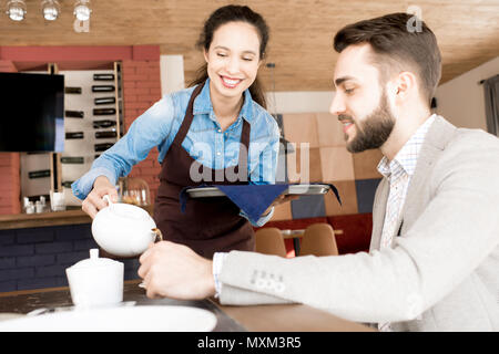 Cheerful waitress pouring tea for customer Stock Photo