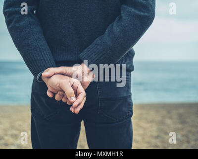 A senior man is standing on the beach with his hands behind his back Stock Photo