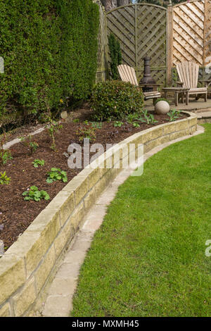 Corner of beautiful, landscaped, private garden with contemporary design, border plants, patio seating, lawn & ornaments - Yorkshire, England, Stock Photo