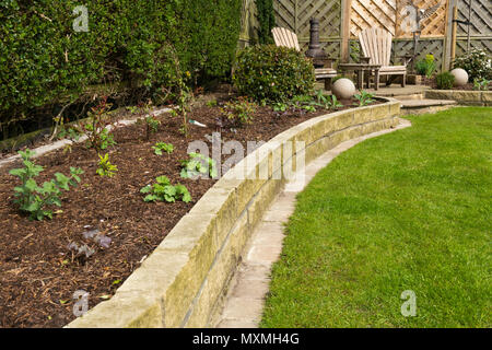 Corner of beautiful, landscaped, private garden with contemporary design, border plants, patio seating, lawn & ornaments - Yorkshire, England, UK. Stock Photo