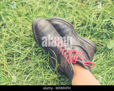 The feet and boots of a young person resting on the grass in nature Stock Photo