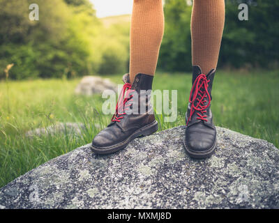 The feet of a young woman wearing boots standing on a rock in nature Stock Photo