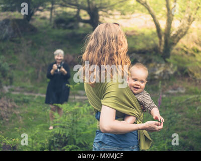 A young mother and her baby in a sling is posing for a picture in the forest Stock Photo