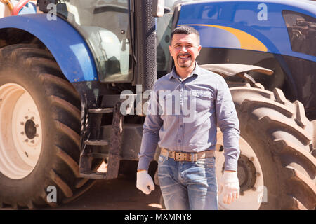 portrait of positive smiling mature male farmer near huge tractor Stock Photo