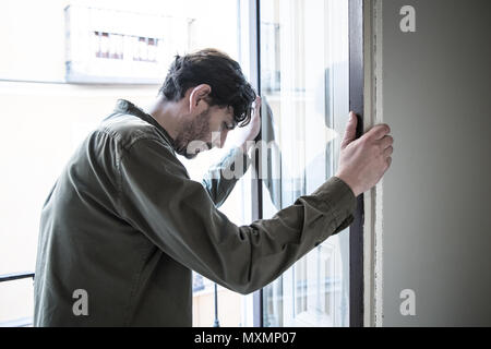 Lonely young man looking outside house balcony looking depressed, destroyed, sad and suffering emotional crisis and grief thinking of taking a difficu Stock Photo