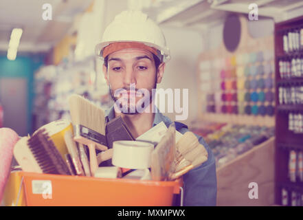 Young workman holding basket with picked tools in paint store Stock Photo