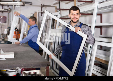 Production smiling english workers in coverall with different    finished PVC profiles and windows at factory Stock Photo