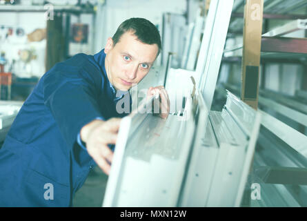 Serious production worker in coverall with different PVC windows and doors Stock Photo
