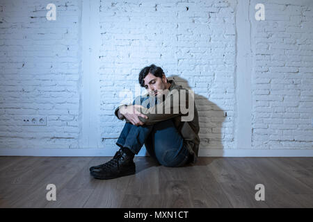 young depressed man sitting against a white wall at home with a shadow on the wall feeling miserable, lonely and sad in mental health depression conce Stock Photo