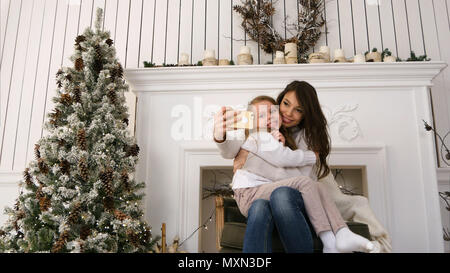 Cheerful young mother and her daughter making comic xmas selfies and showing tongues Stock Photo